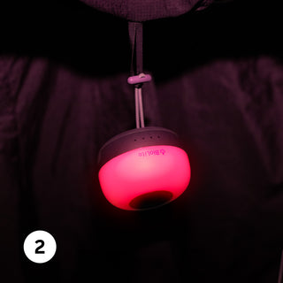A hanging light with a soft red glow, featuring a gray top and a strap, against a dark background.