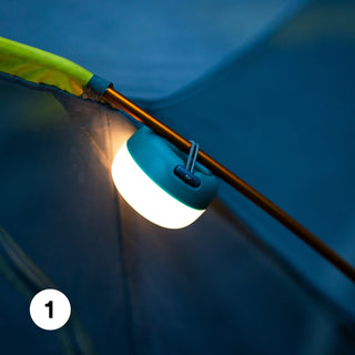 A camping lantern is hanging inside a tent, illuminating the space with a soft glow.
